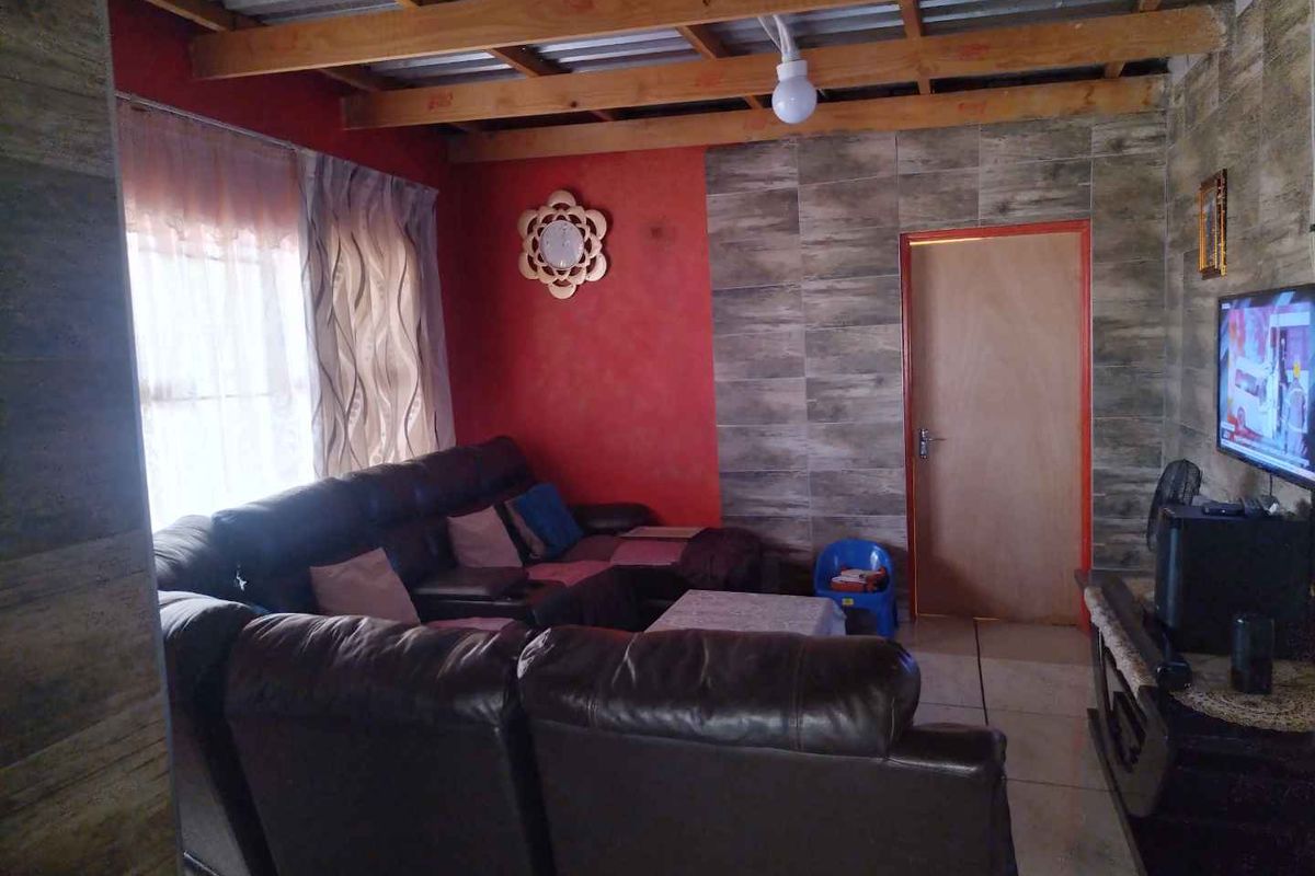 Living room featuring tiled flooring, exposed timber ceiling rafters, and a combination of textured wall finishes.