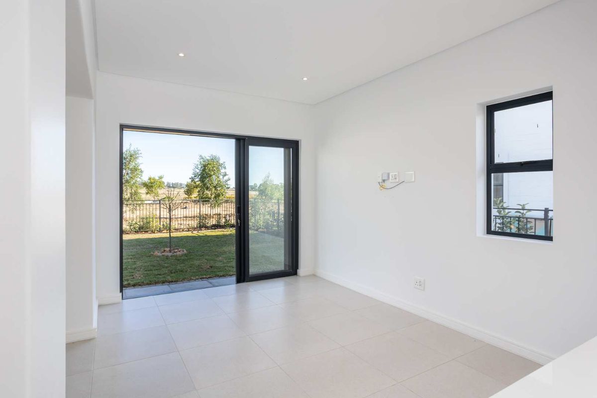A bright, modern living area featuring neutral floor tiles, recessed ceiling lighting, and large sliding glass doors opening to a private garden.