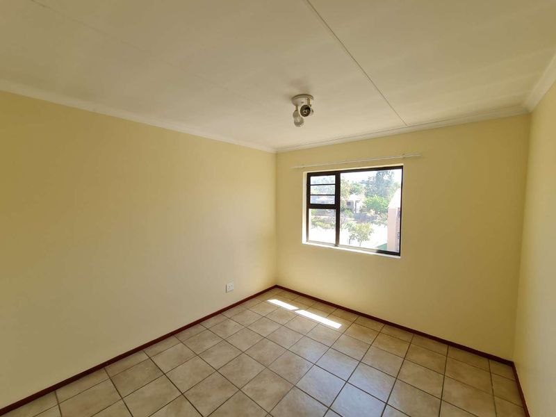 A bright, empty bedroom featuring neutral walls, tiled flooring, and an aluminium-framed window providing natural light.
