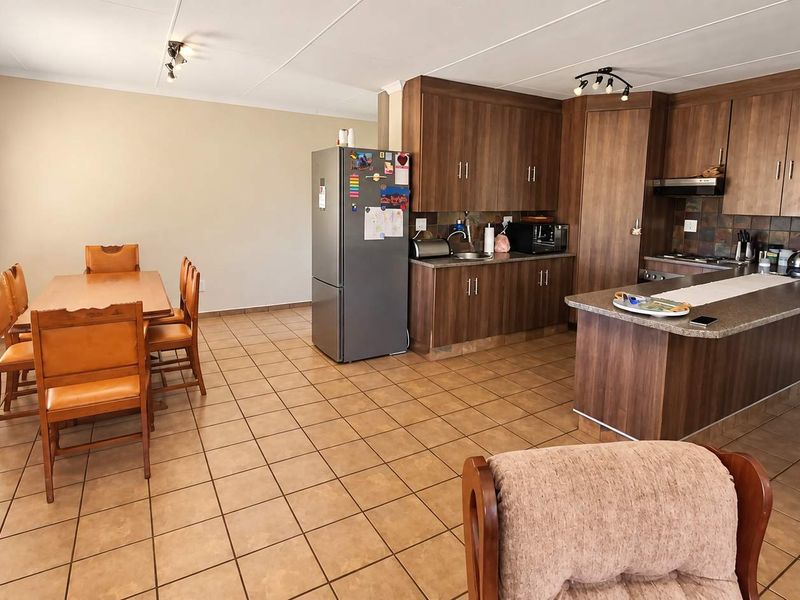 Open-plan kitchen and dining area featuring wood-finish cabinetry, a central island, tiled flooring, and functional built-in kitchen appliances.