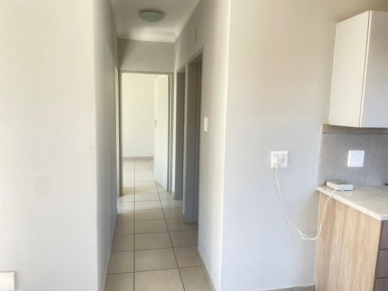 A clean, neutral hallway featuring tiled flooring and access to adjacent rooms, with a partial view of kitchen cabinetry on the right.