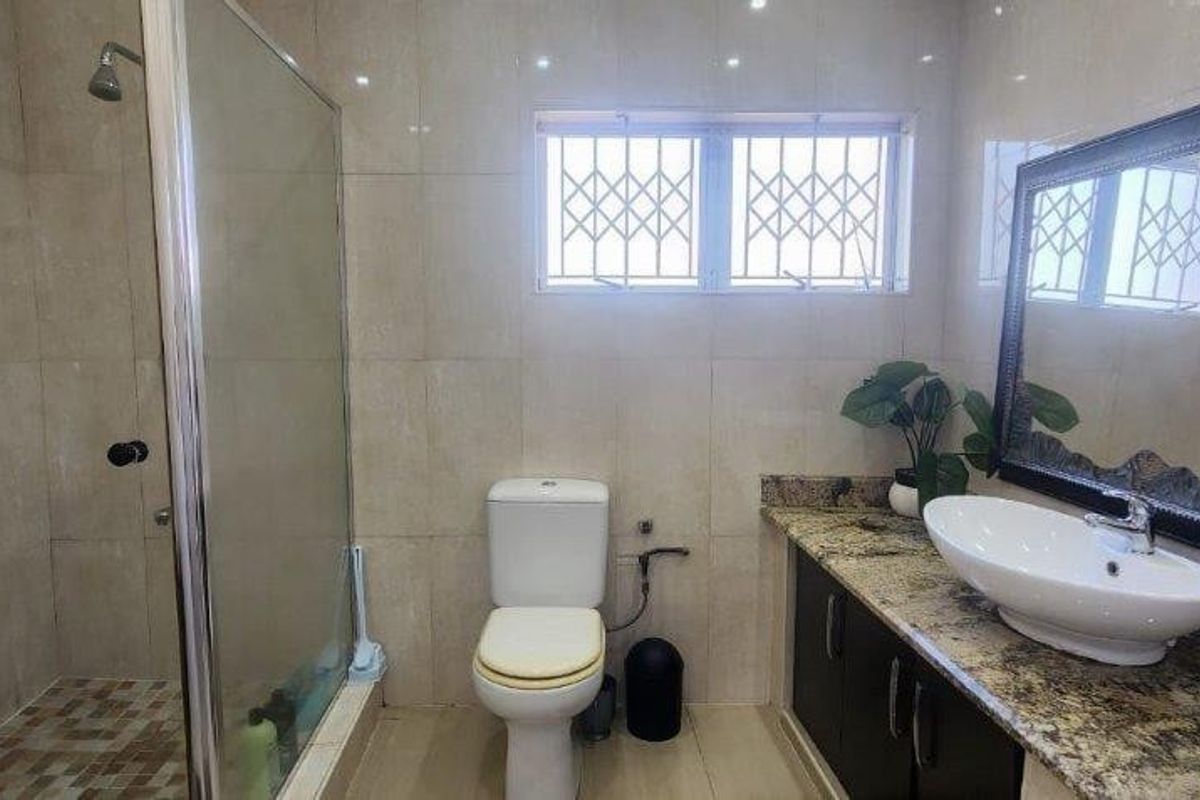 A well-maintained bathroom featuring a glass-enclosed shower, granite vanity countertop with a vessel sink, and neutral wall tiling.