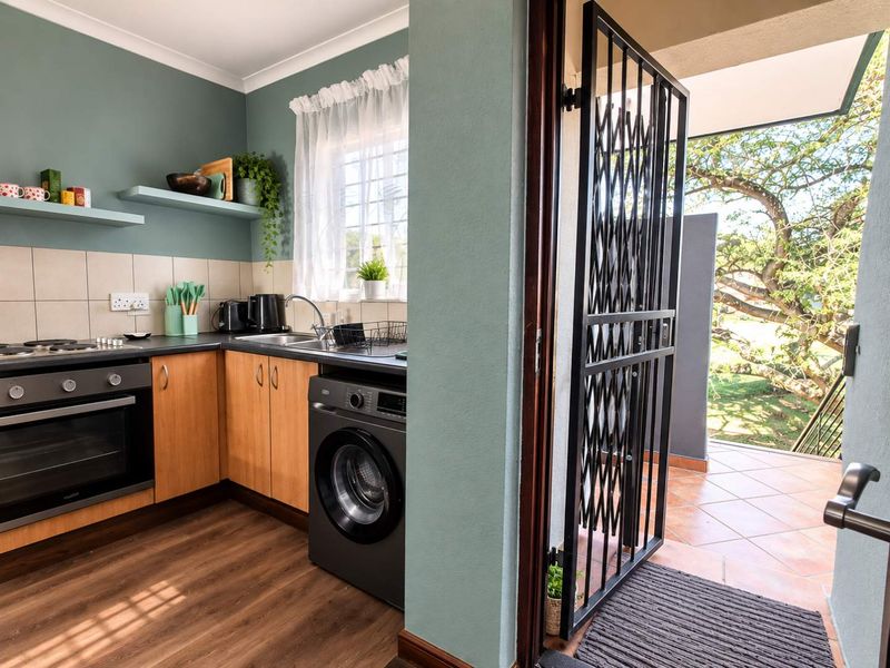 A functional kitchen featuring wood-finish cabinetry, a built-in oven, hob, and direct access to an outdoor patio area through a security gate.