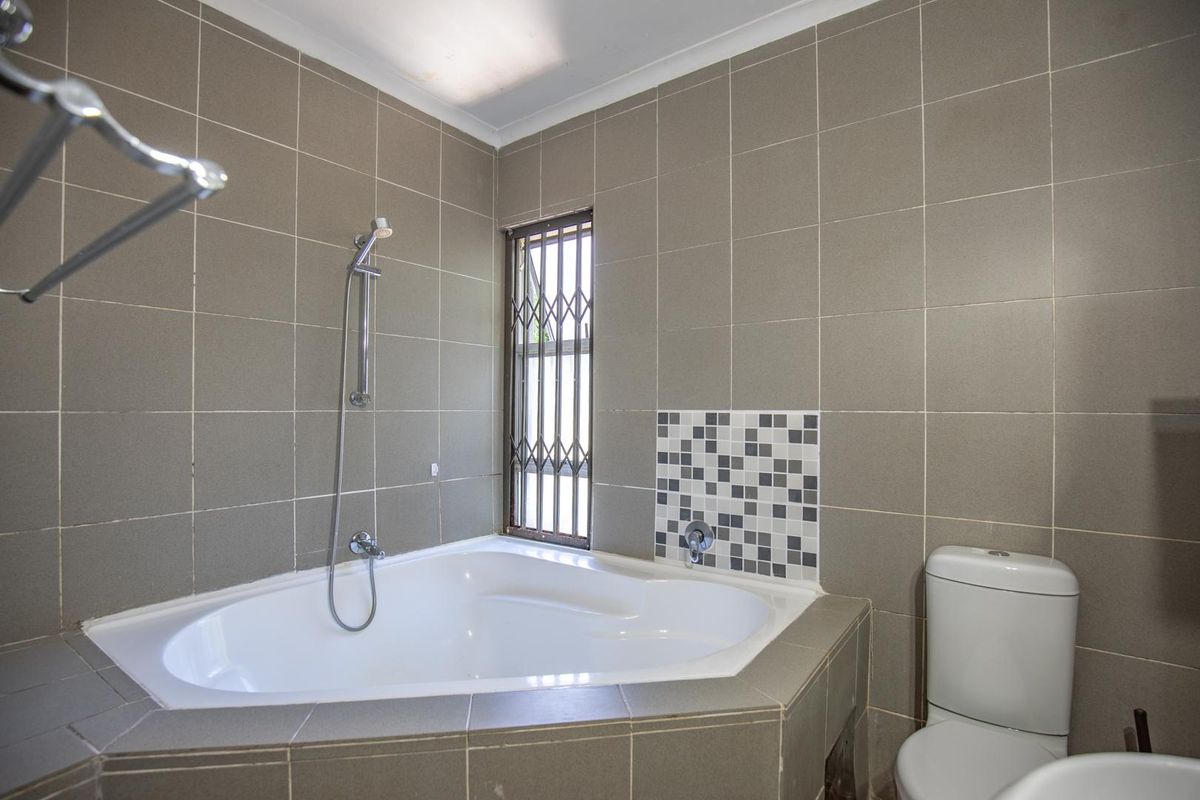 A bathroom featuring a corner bathtub with a handheld showerhead, a toilet, and neutral wall tiling with a decorative mosaic accent.