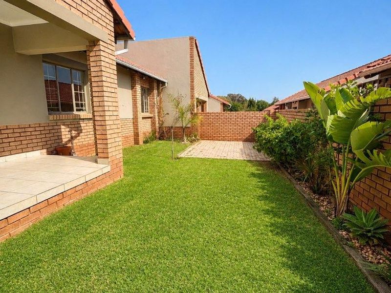 A well-maintained rear garden featuring a brick facade, a covered tiled patio, a paved section, and a neat lawn enclosed by brick boundary walls.
