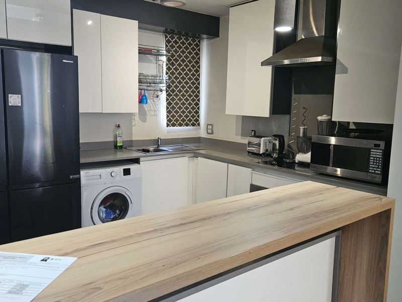 Modern kitchen featuring sleek white cabinetry, stone countertops, a breakfast bar, and integrated laundry facilities, offering a functional and contemporary cooking space.