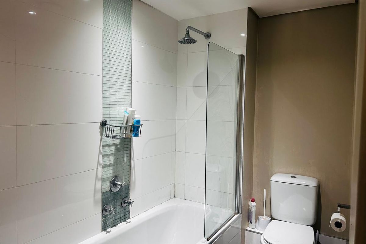 A functional bathroom featuring a bathtub with a glass shower screen, a mosaic tile accent wall, and a standard toilet.