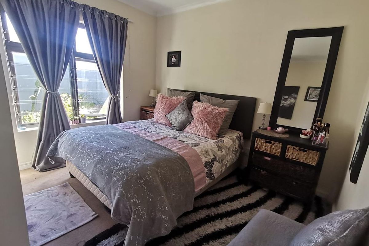 A well-lit bedroom featuring neutral wall tones, carpeted flooring, and a large window providing natural light.