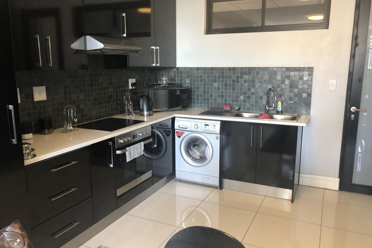 Modern kitchen featuring high-gloss black cabinetry, stone countertops, mosaic tile backsplash, integrated oven, hob, and a double bowl sink with porcelain tiled flooring.