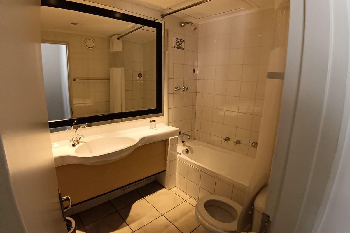 A functional bathroom featuring a built-in bathtub with shower overhead, a vanity basin with large mirror, and tiled flooring.