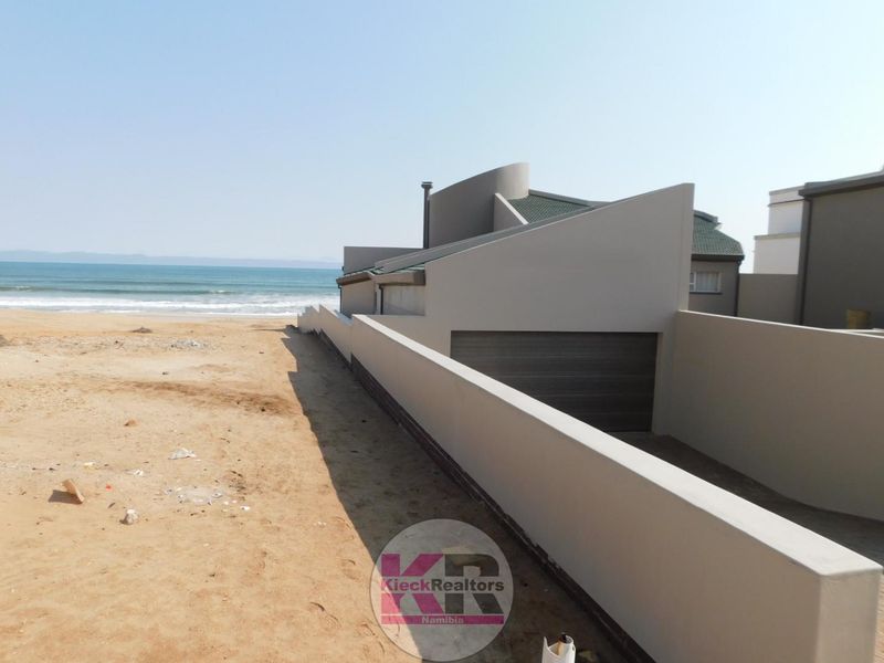 Rear view of the property featuring a modern architectural design, boundary wall, and direct access to the beach.