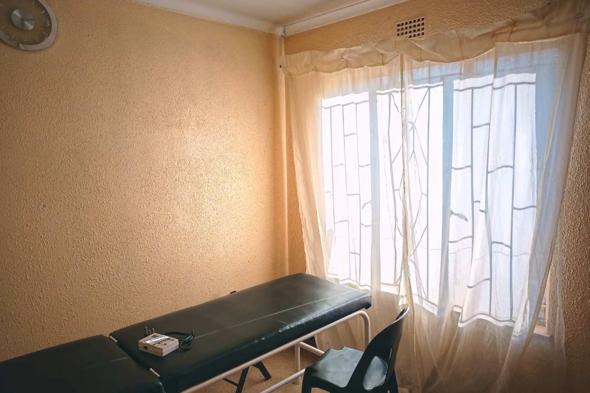 A bedroom space featuring textured walls and a window fitted with security bars, currently utilized as a treatment room.