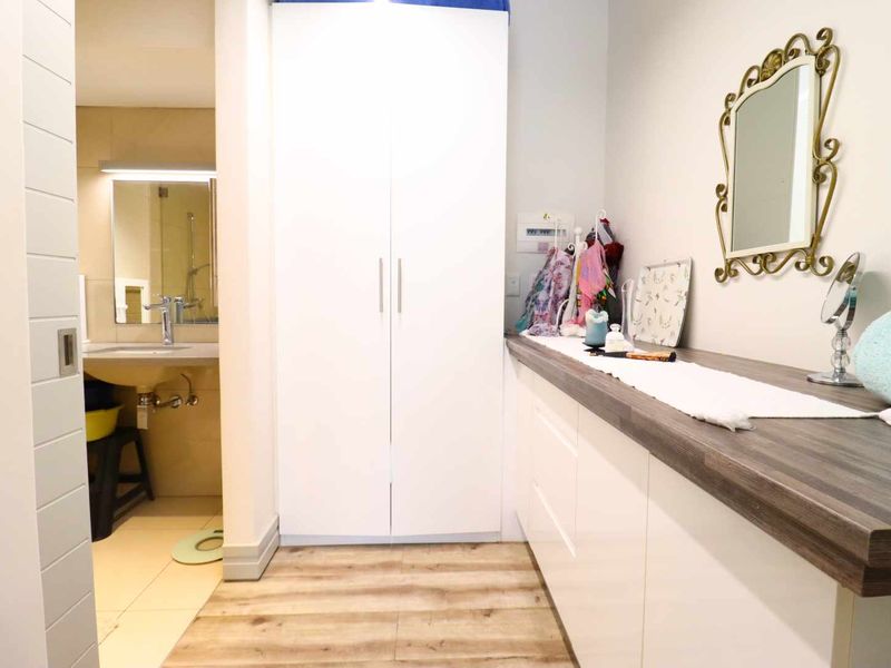 A modern bathroom area featuring a wall-mounted basin, extensive built-in cabinetry with a wood-look countertop, and a tall built-in wardrobe for storage.