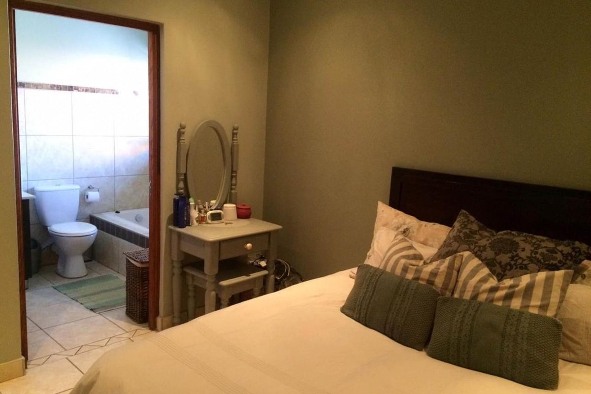 A bedroom featuring an en-suite bathroom with a bathtub and toilet, finished with neutral wall tones and tiled flooring.