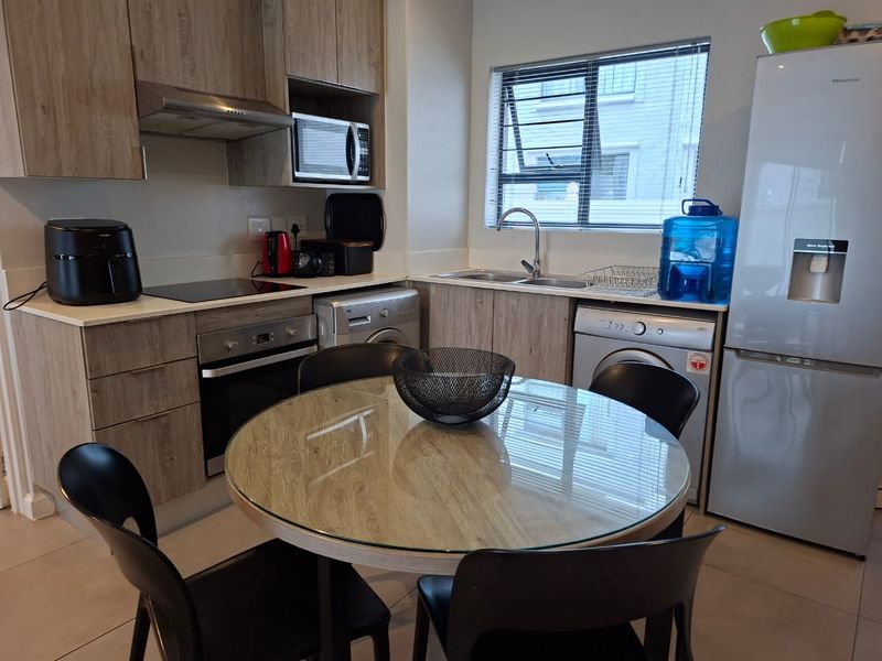 Modern open-plan kitchen featuring wood-finish cabinetry, integrated appliances, and tiled flooring, seamlessly connected to a dining area.