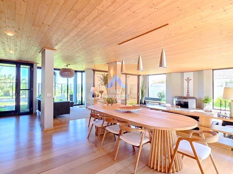 Spacious open-plan living and dining area featuring warm timber ceilings, hardwood flooring, a built-in fireplace, and expansive glass doors leading to the outdoors.