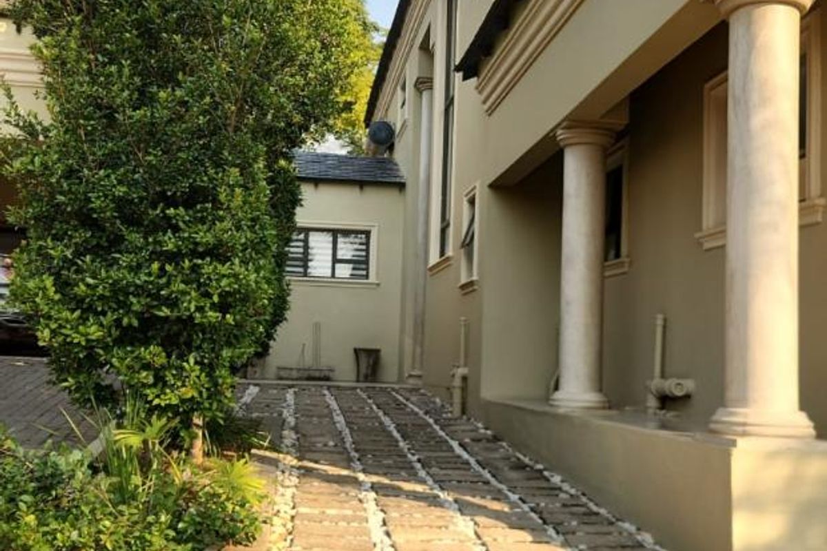 Side exterior view of the property featuring a paved walkway, decorative stone accents, and classic architectural columns along the building facade.