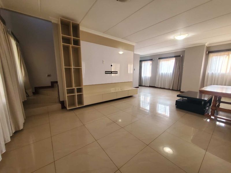 Spacious living area featuring large format floor tiles, a custom built-in media wall unit, and an integrated staircase leading to the upper level.