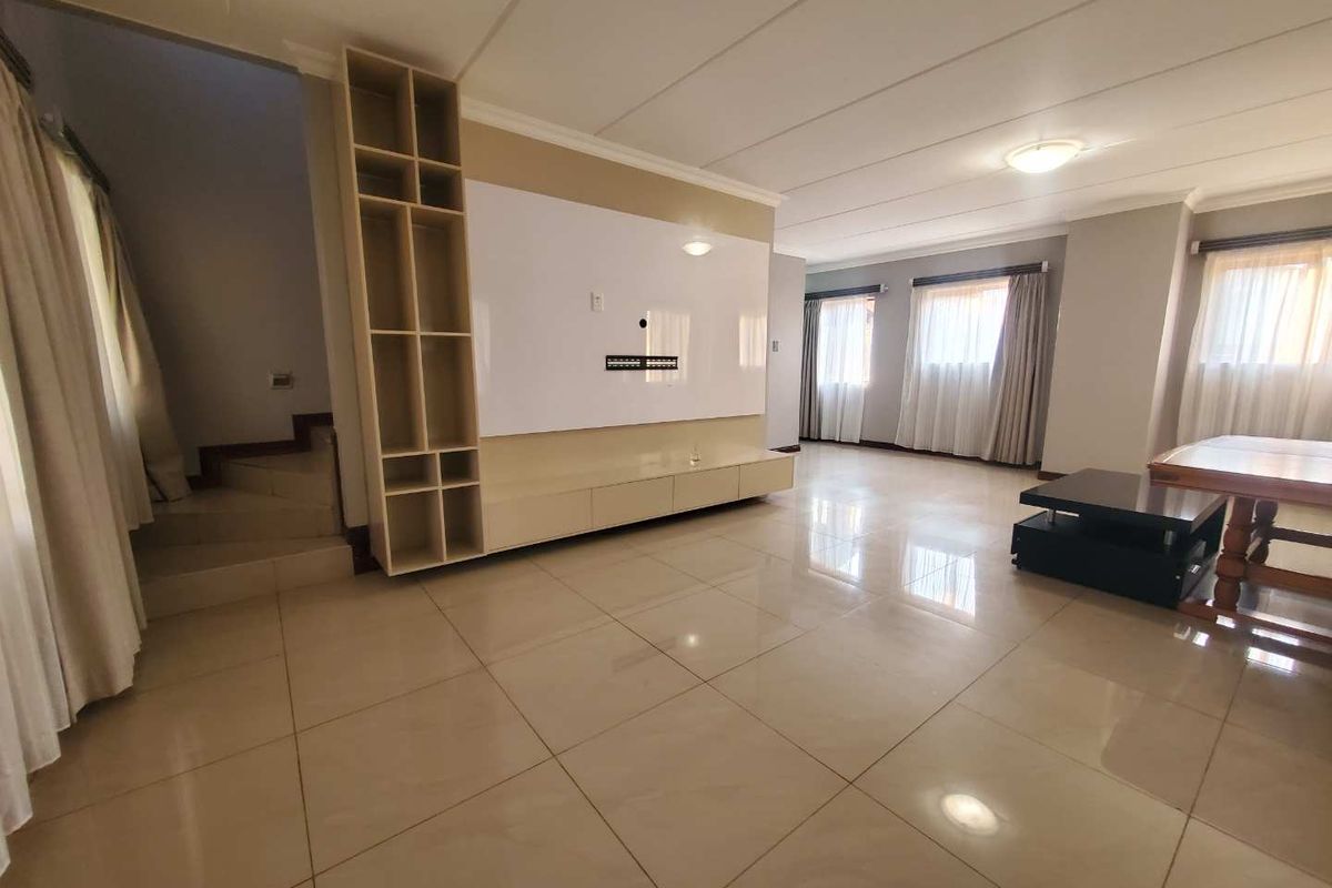 Spacious living area featuring large format floor tiles, a custom built-in media wall unit, and an integrated staircase leading to the upper level.