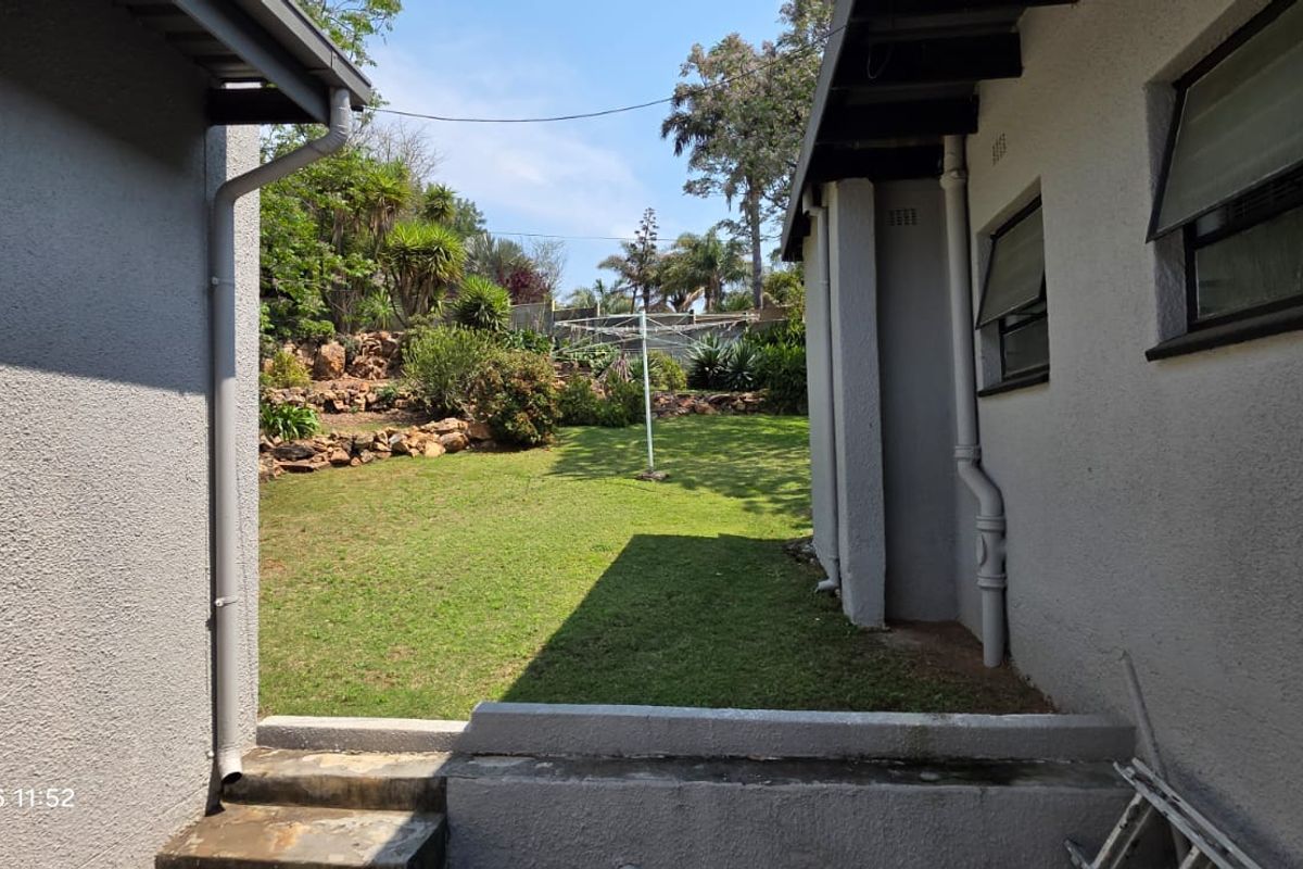 A view of the rear garden area featuring a lawn, retaining wall, and exterior building walls with installed downpipes and windows.