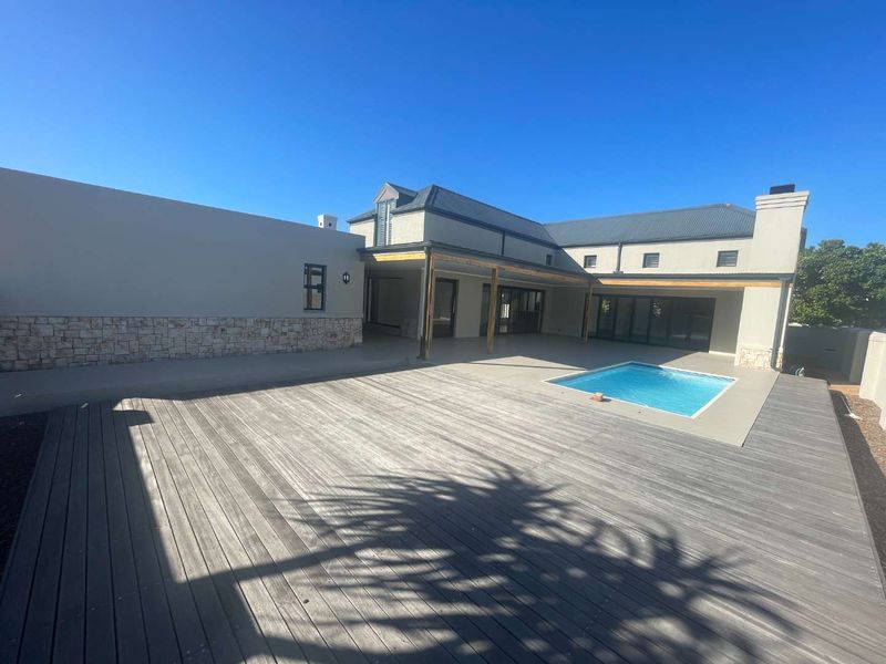 Spacious rear exterior featuring a large timber deck, covered patio area, and a swimming pool set against the modern residence.