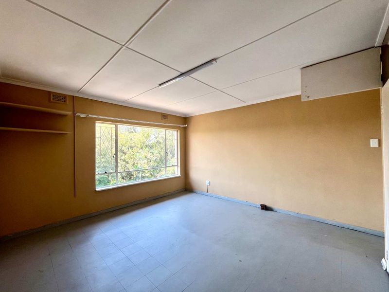 An empty bedroom featuring tiled flooring, built-in shelving, and a large window, offering a blank canvas for renovation and interior design.