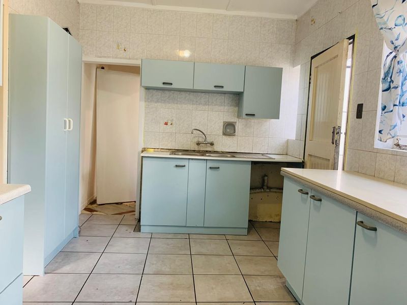 A dated kitchen featuring light blue cabinetry, tiled splashbacks, and tiled flooring, requiring some maintenance and cosmetic updates to modernize the space.