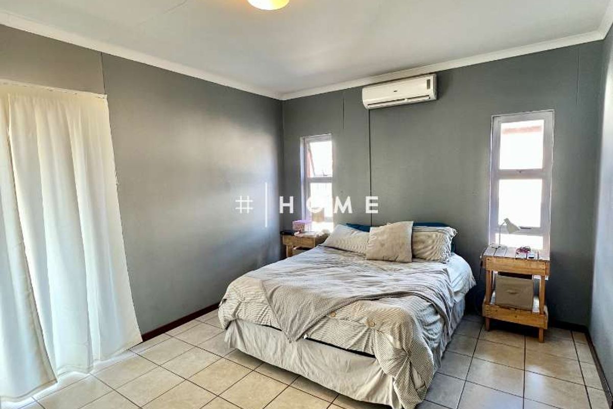 A bedroom featuring tiled flooring, a wall-mounted air conditioning unit, and dual windows providing natural light.