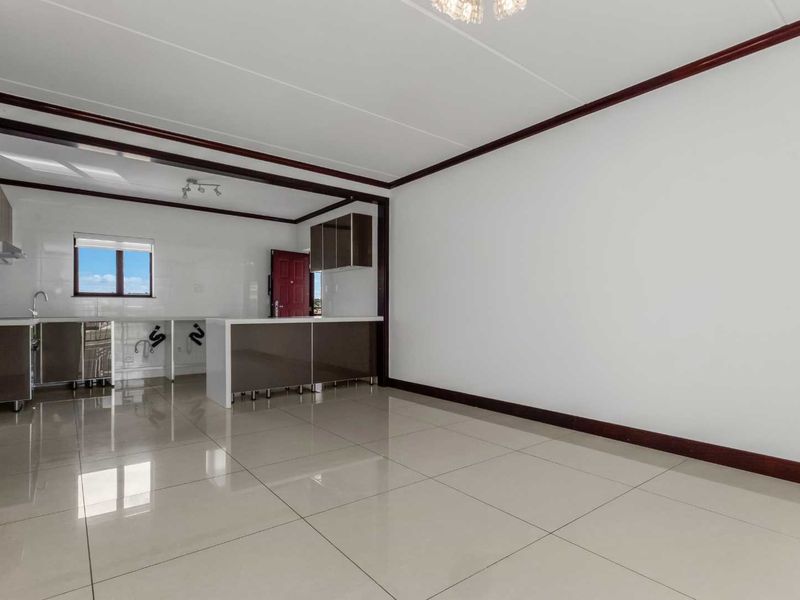 An open-plan living and kitchen area featuring modern tiled flooring, dark-toned cabinetry, and a functional kitchen island in a bright, vacant space.