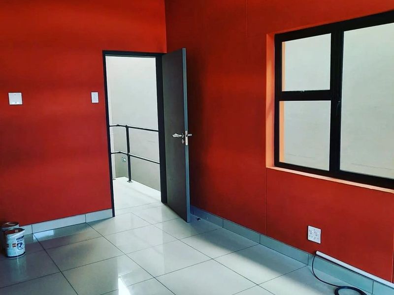 A bright, empty office space featuring vibrant red walls, polished tiled flooring, and a black-framed window, providing a clean and functional workspace.