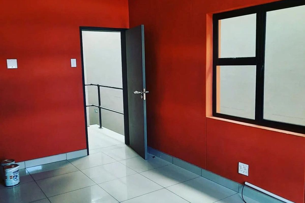 A bright, empty office space featuring vibrant red walls, polished tiled flooring, and a black-framed window, providing a clean and functional workspace.