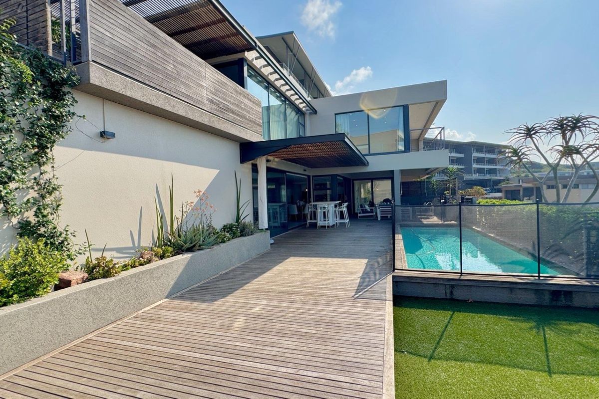 Modern rear exterior featuring a timber deck, swimming pool with glass fencing, raised concrete planters, and a covered patio area.