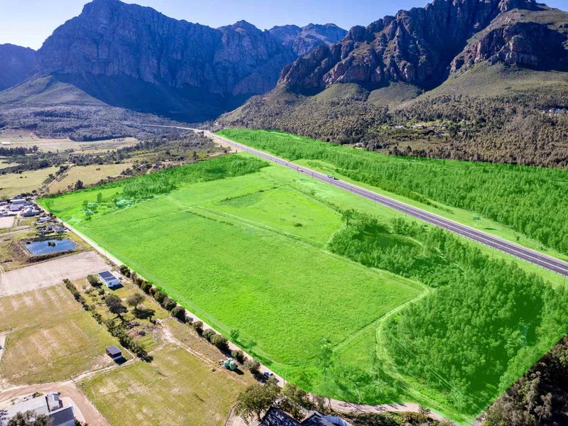 An aerial view of a large, open farm property featuring expansive green fields, mountain views, and direct access to a main road.