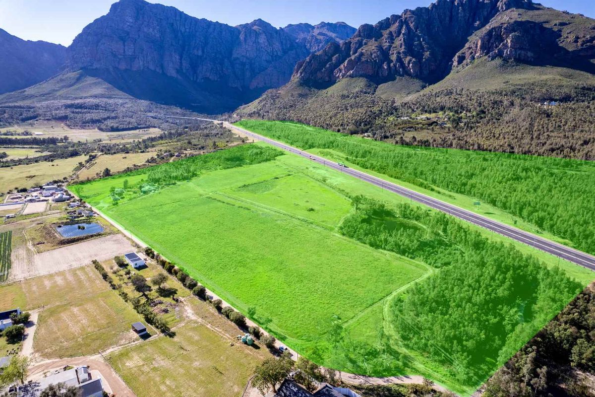 An aerial view of a large, open farm property featuring expansive green fields, mountain views, and direct access to a main road.