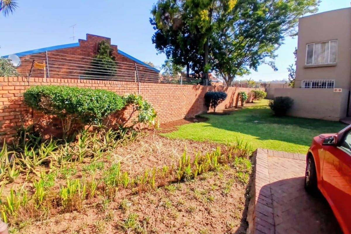 A rear garden area featuring a brick boundary wall, established lawn, landscaped garden beds, and a paved driveway section.