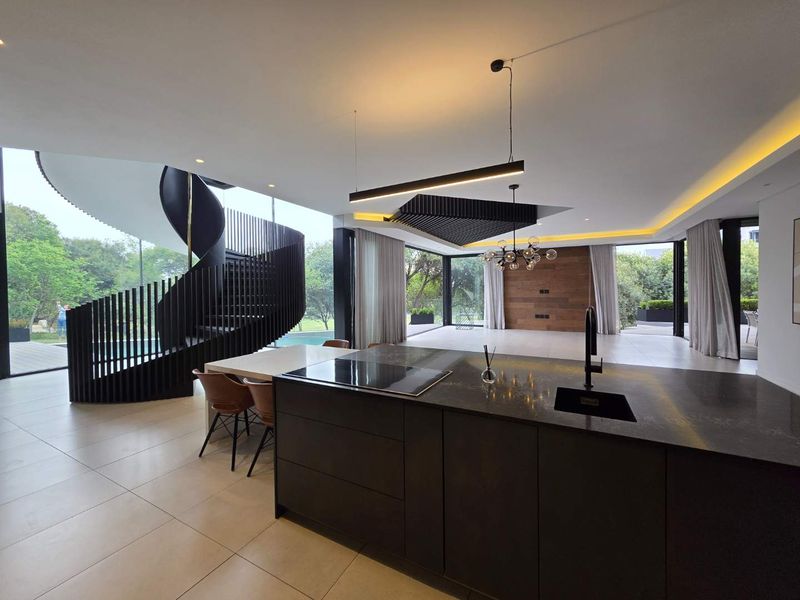 Modern open-plan living area featuring a striking spiral staircase, a sleek kitchen island with integrated cooktop, and expansive floor-to-ceiling windows overlooking the garden.