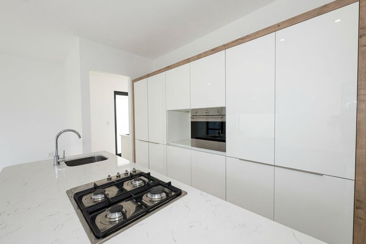 Modern kitchen featuring sleek white cabinetry, stone countertops, a central island with a built-in gas cooktop, and integrated oven.