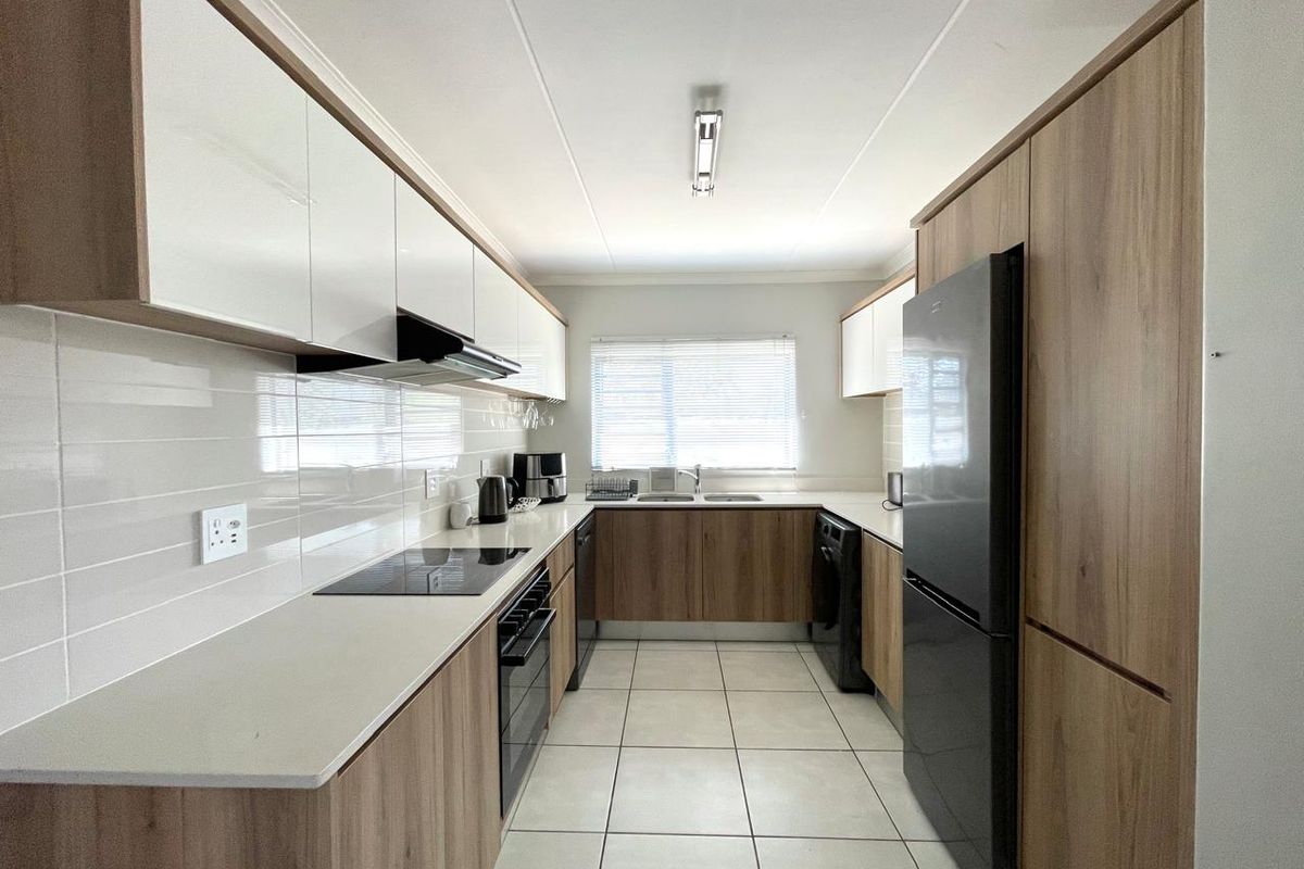 Modern galley-style kitchen featuring wood-grain cabinetry, white high-gloss upper cabinets, stone countertops, integrated hob, oven, and tiled flooring.