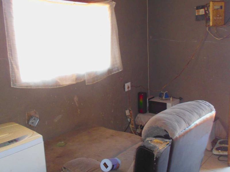 A utility space featuring tiled flooring and an exposed electrical distribution board, requiring significant wall repairs and cosmetic updates.