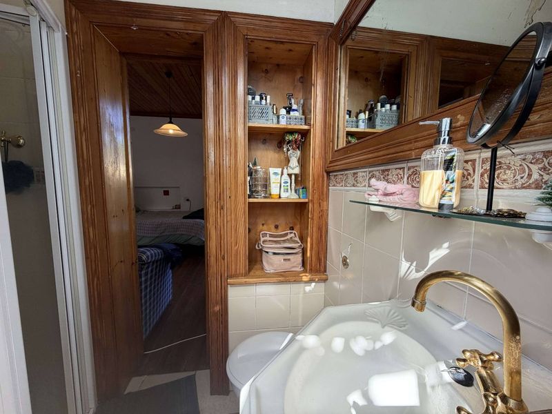 Bathroom featuring built-in wooden shelving, a pedestal basin with brass fixtures, and ceramic wall tiling, with an adjacent view into the bedroom.