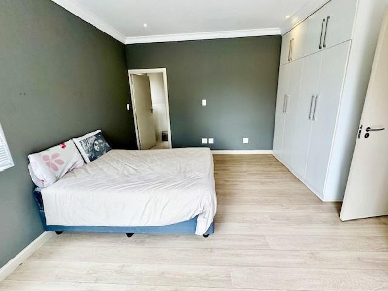 Spacious bedroom featuring light-toned laminate flooring, modern built-in cupboards, and neutral dark-toned walls with recessed lighting.