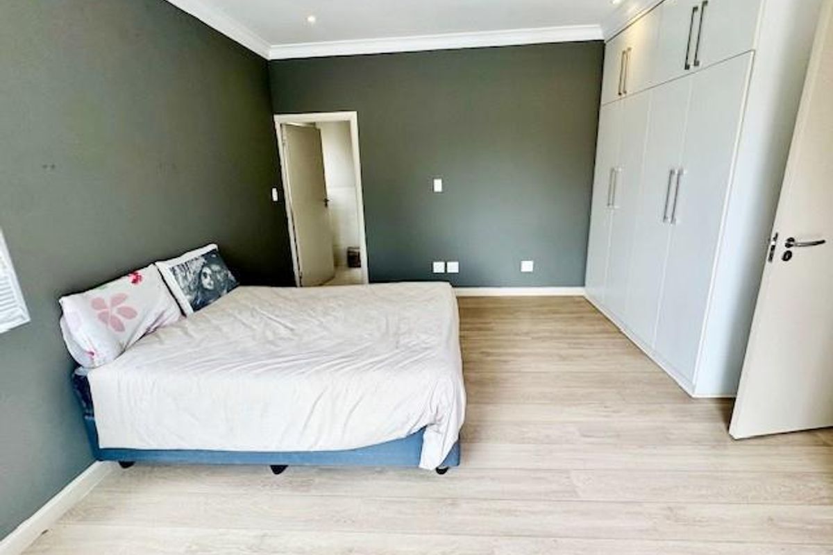 Spacious bedroom featuring light-toned laminate flooring, modern built-in cupboards, and neutral dark-toned walls with recessed lighting.