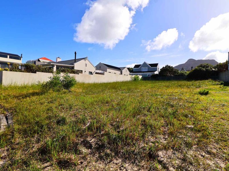 A vacant residential plot featuring natural grass cover, enclosed by boundary walls, situated in a developed neighborhood with mountain views.