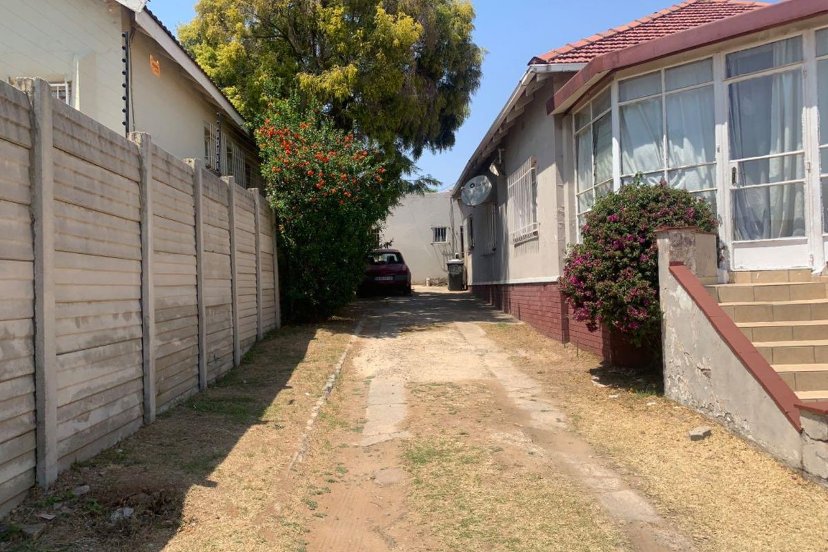 A side driveway view showing the exterior wall of the house, concrete boundary wall, and access path leading to the rear of the property.