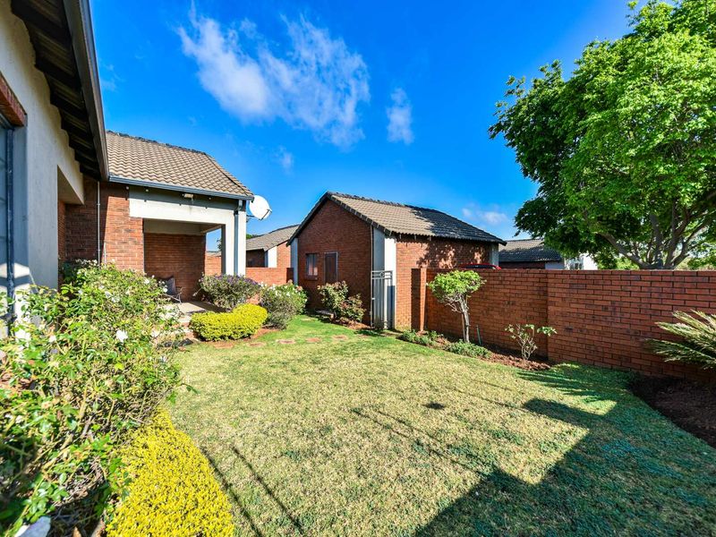 A well-maintained rear garden featuring a lawn, brick boundary walls, and a covered patio area attached to the townhouse structure.