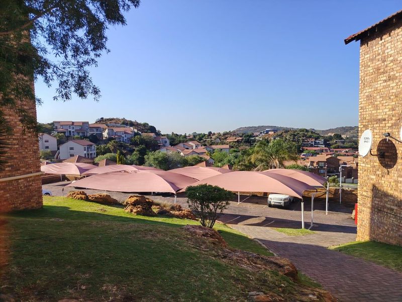 View of the complex parking area featuring shade cloth carports, paved driveway, and surrounding residential buildings.