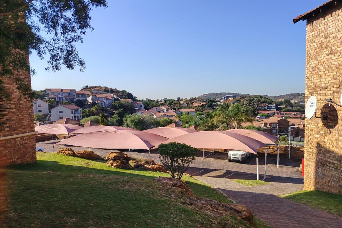 View of the complex parking area featuring shade cloth carports, paved driveway, and surrounding residential buildings.