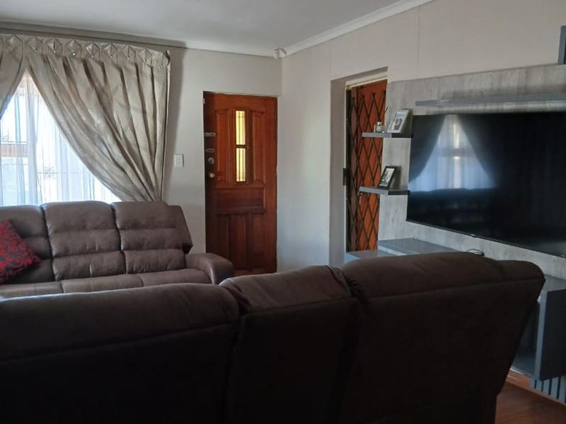 A comfortable living room featuring laminate flooring, a built-in media unit, and a timber entrance door with security gate access.