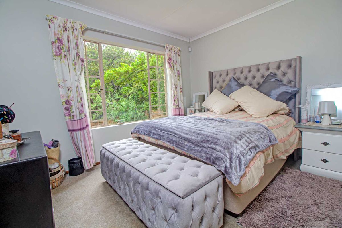 A well-lit bedroom featuring neutral wall tones, carpeted flooring, and a large window providing natural light and garden views.
