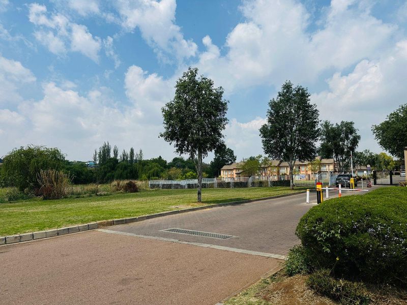 View of the apartment complex entrance featuring a paved driveway, security boom gate, and landscaped surroundings.